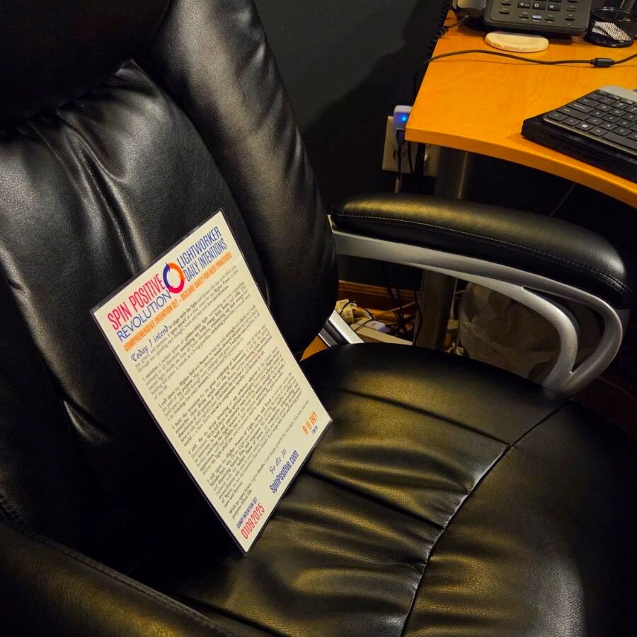 A laminated copy of the Spin Positive Revolution Intention Set sits on an office chair behind a desk with a computer keyboard and desk phone.