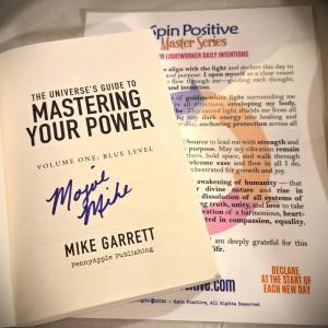 A picture of a signed copy of Volume #1 of the Spin Positive Master Series opened to the title page where the signature is found. It is laying on top of a printed laminated heavy-duty Master Series Warrior Lightworker Daily Intention Set.